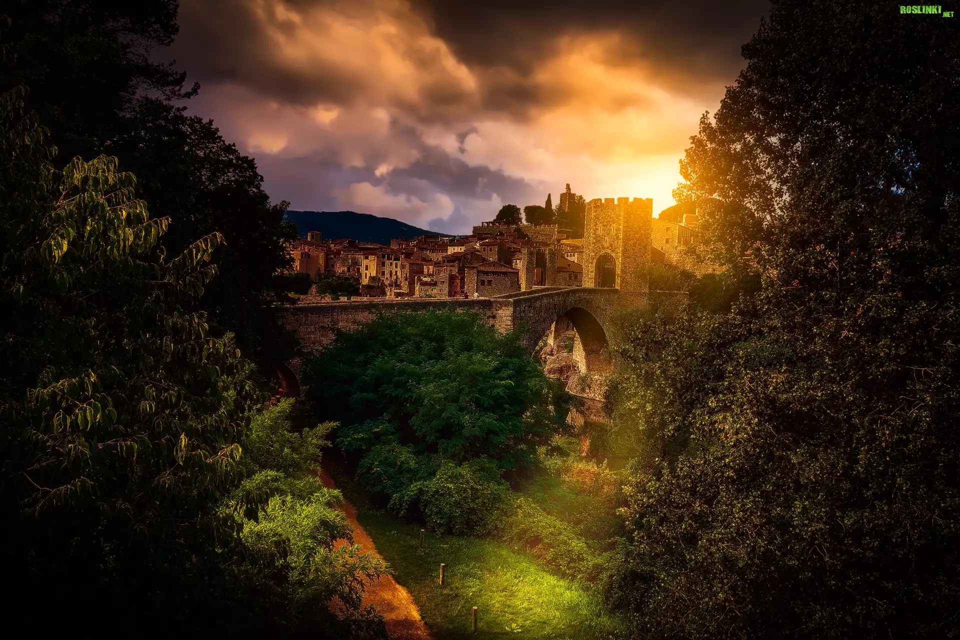 Hiszpania, Miejscowość Besalu, Most Puente de Besalu, Domy, Wzgórza, Drzewa, Roślinność, Wschód słońca, Chmury